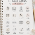 Une femme souriante feuillette son Bullet Journal avec des stylos colorés sur la table